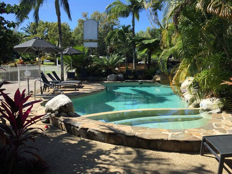 A pool area with lounge chairs, umbrellas, and tropical plants.