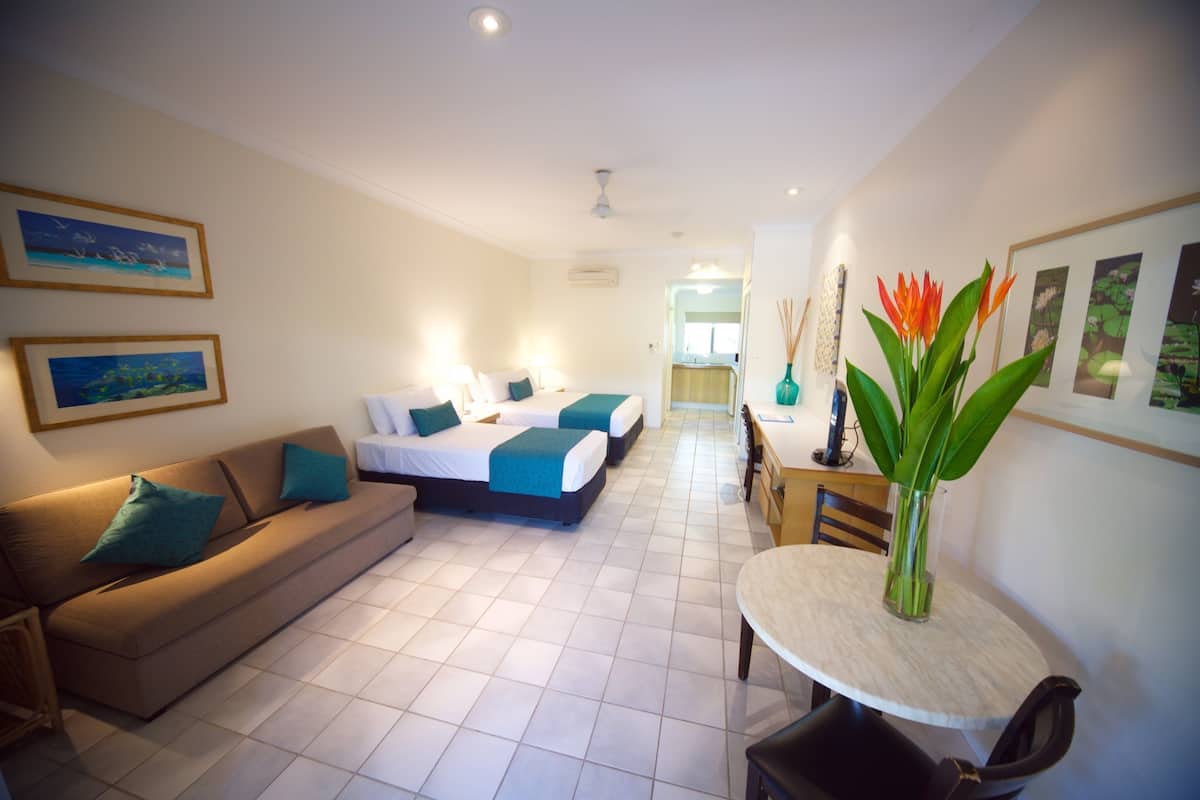 A hotel room with a sofa, two beds, a dining table, and artwork on the walls.