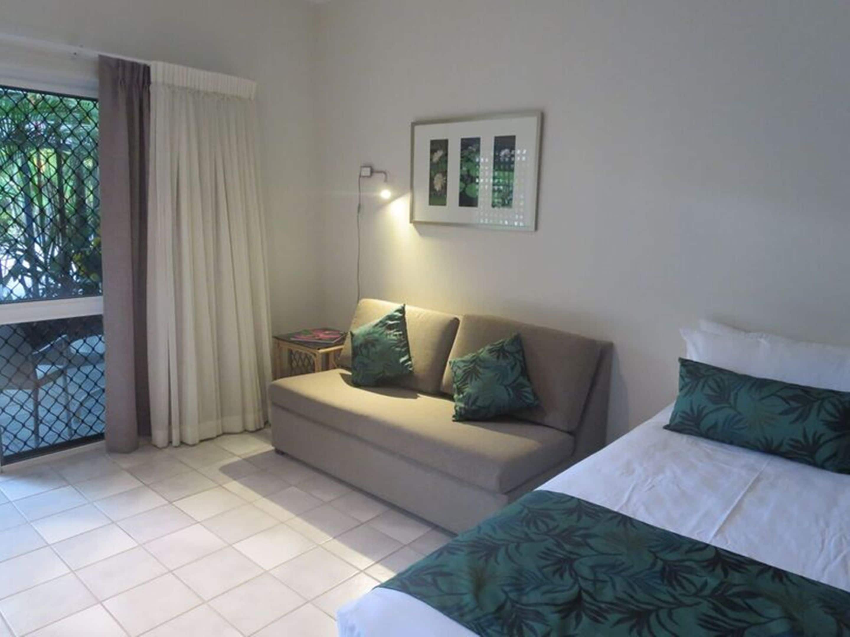 A hotel room with a bed, a sofa, a small table, and a window with curtains.