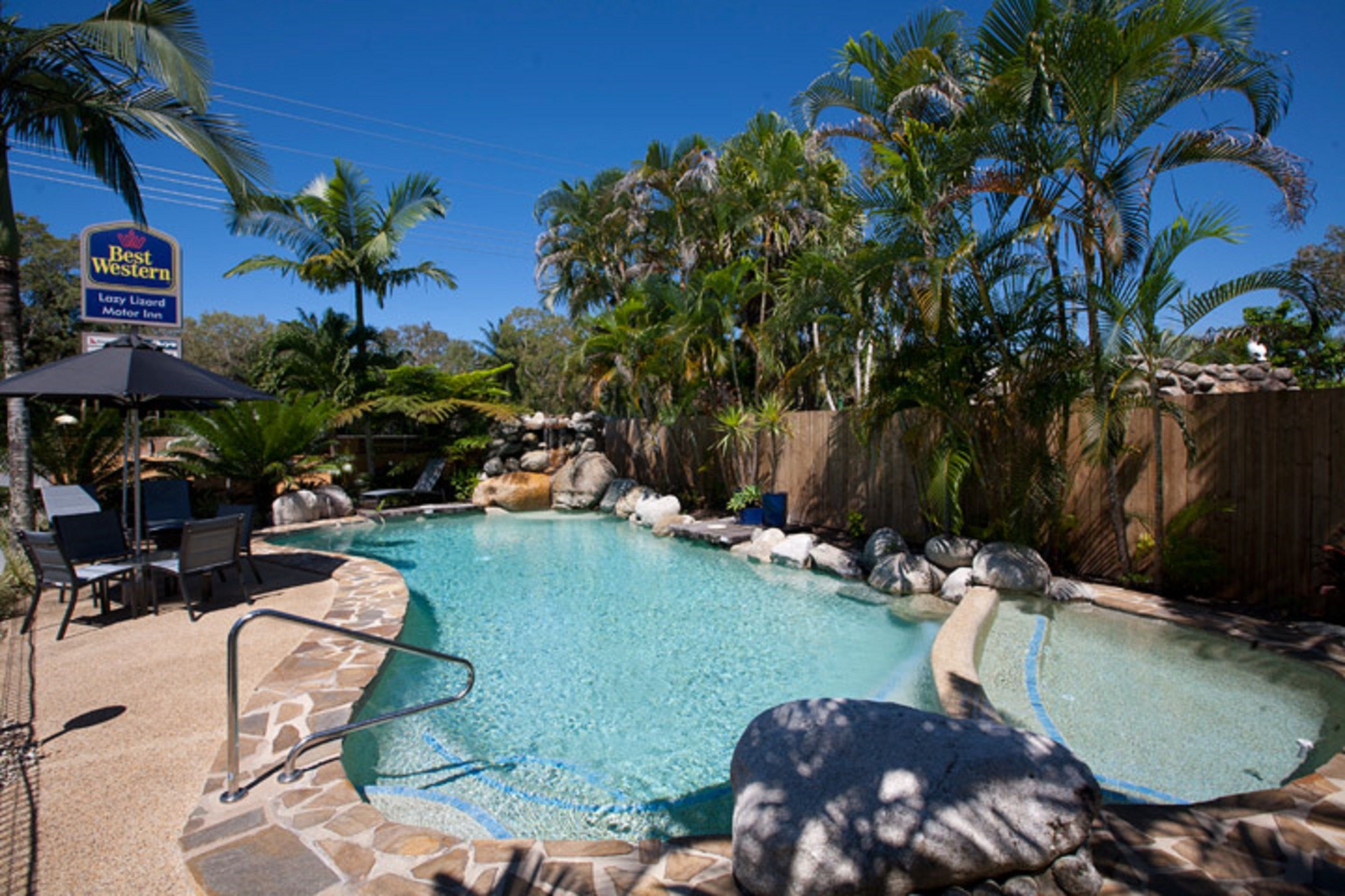 A pool area with lounge chairs, a sign for Best Western, and palm trees.