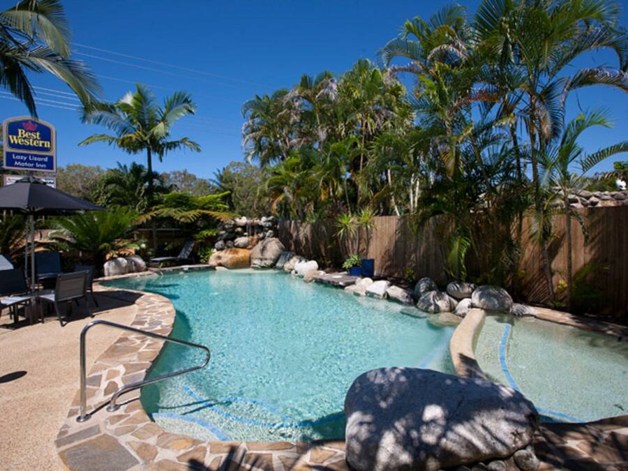 A pool area with lounge chairs, a sign for Best Western, and palm trees.