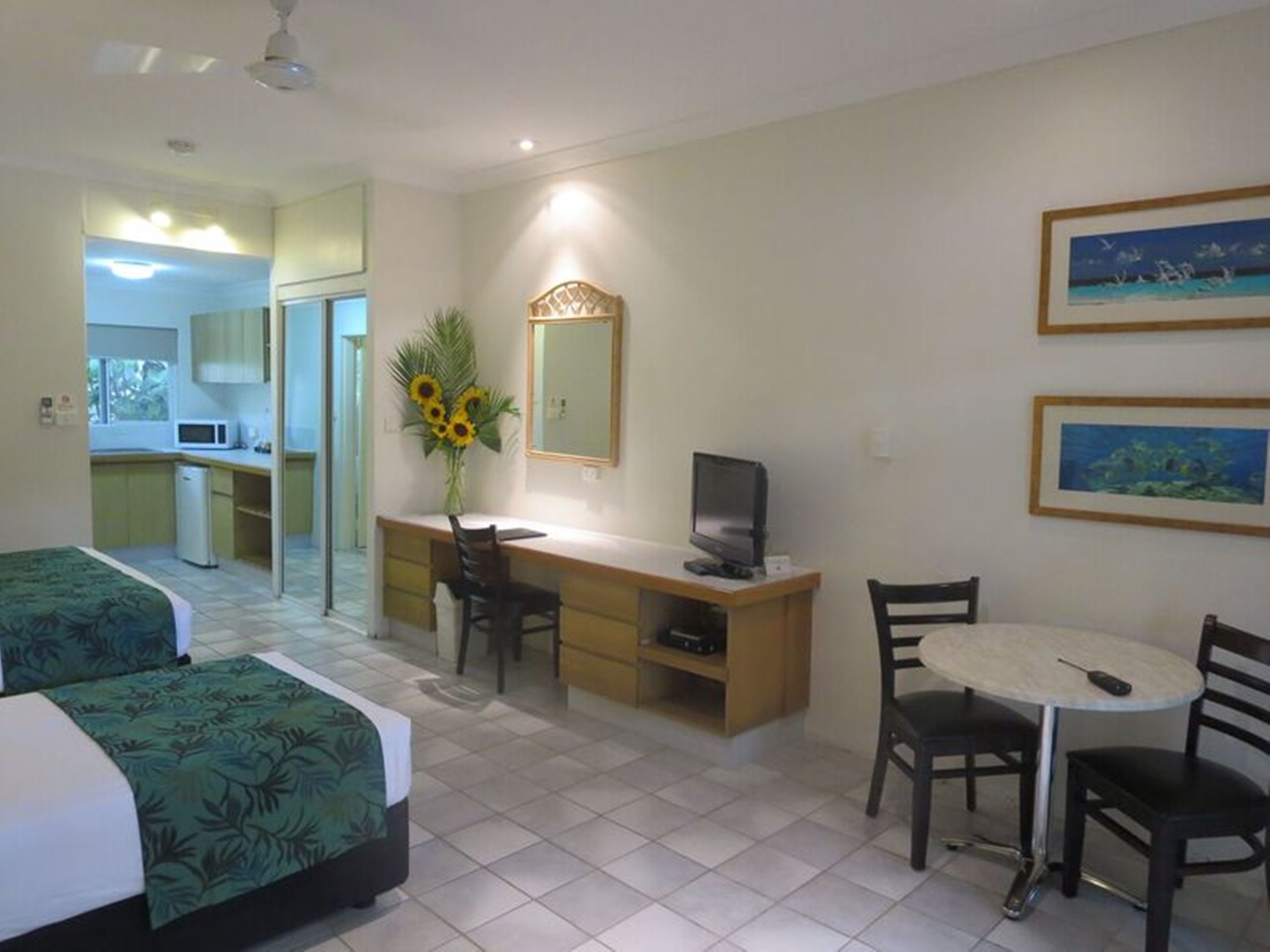 A hotel room with two beds, a desk with a computer, a small table, and chairs. There is a mirror above the desk and a painting on the wall.