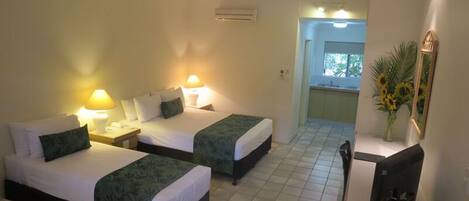 A hotel room with two beds, a desk, a chair, a TV, and a bathroom visible through an open door.