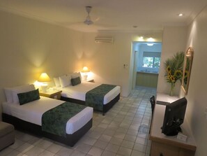 A hotel room with two beds, a desk, a chair, a TV, and a bathroom visible through an open door.