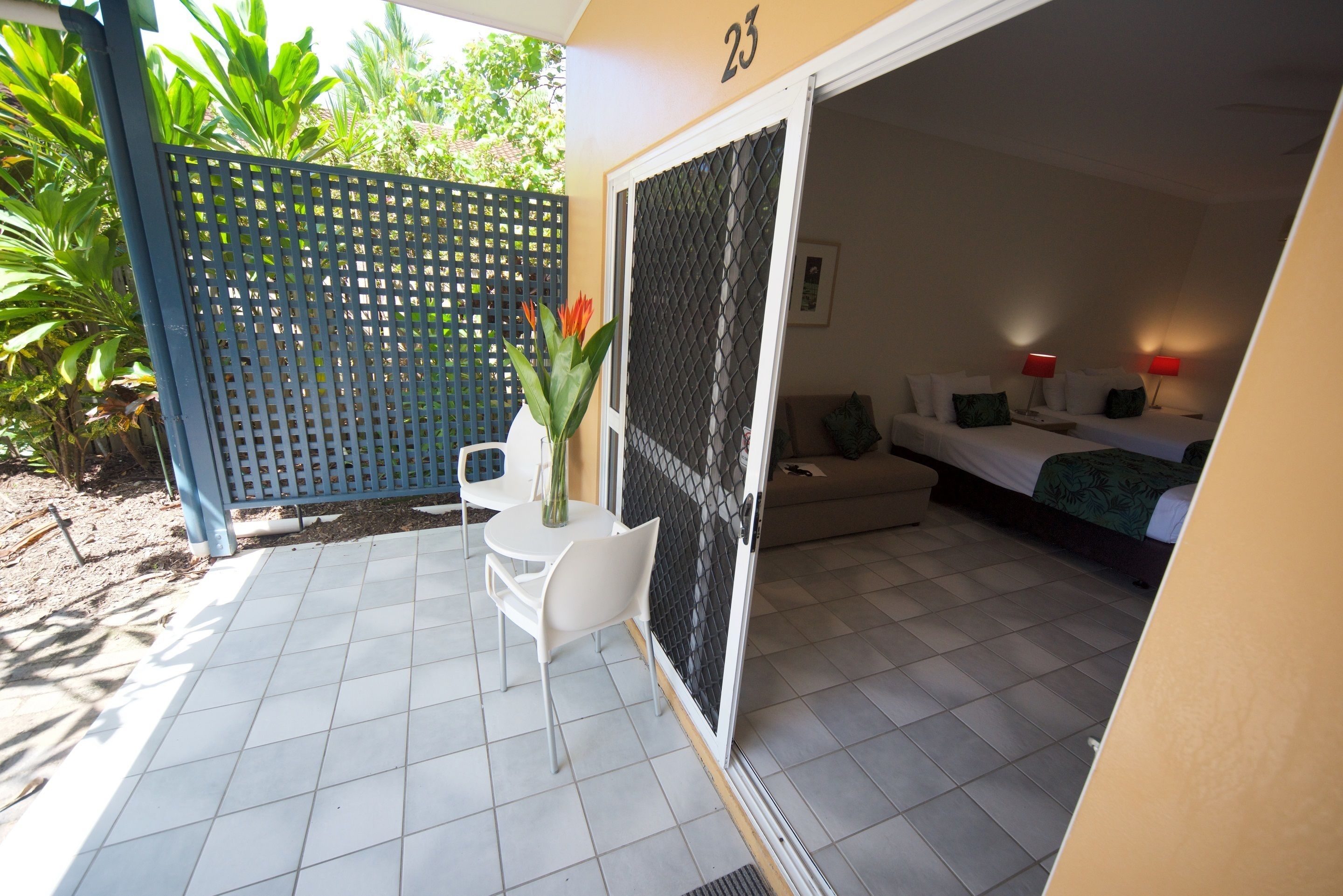 A room with a bed, a small table with chairs, a potted plant, and a sliding door leading to a balcony.