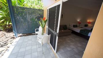 A room with a bed, a small table with chairs, a potted plant, and a sliding door leading to a balcony.