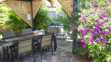 An outdoor patio with a table and chairs, a grill, and lush greenery.