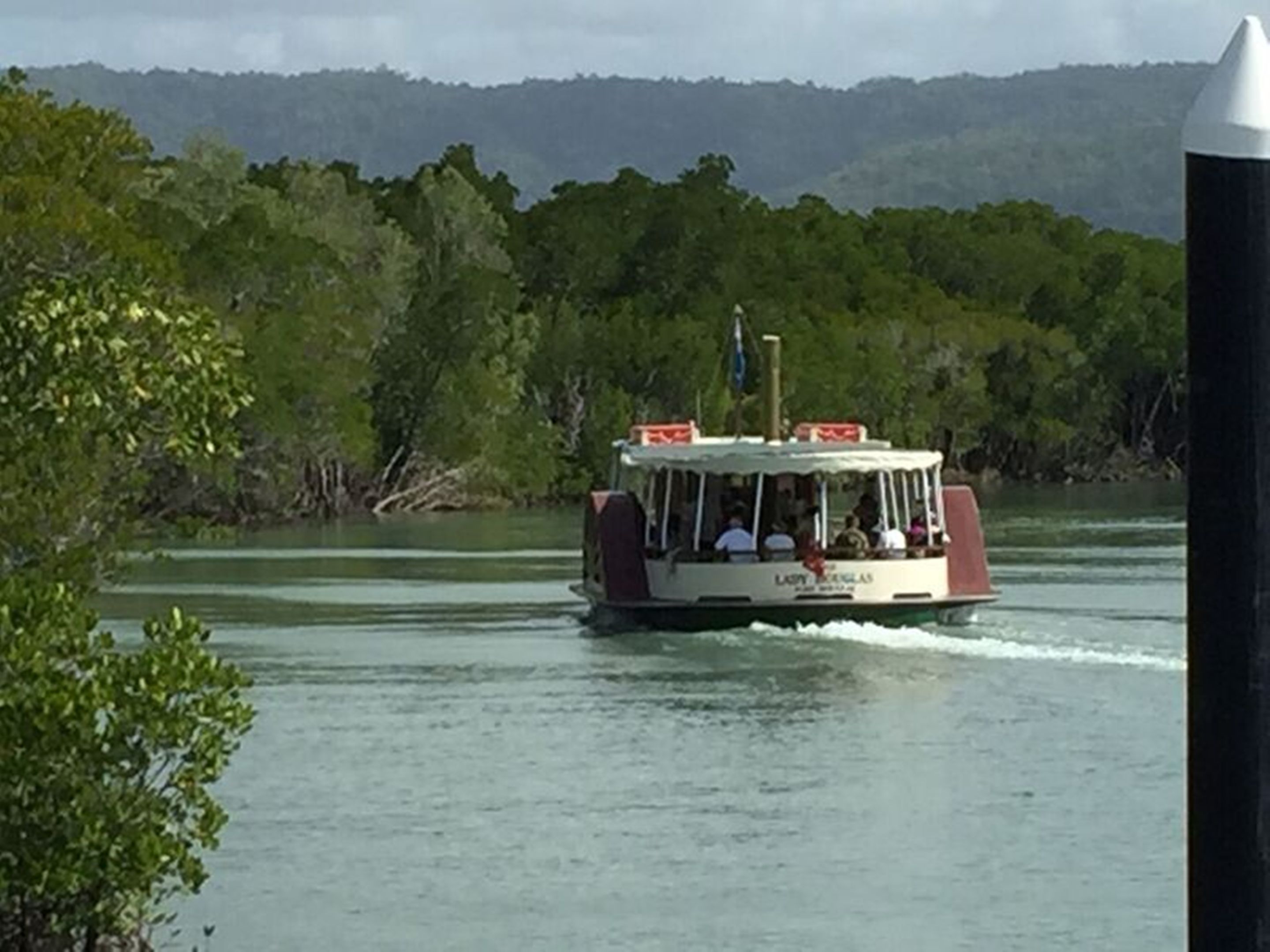 A boat with passengers, moving on a body of water with a forested background.