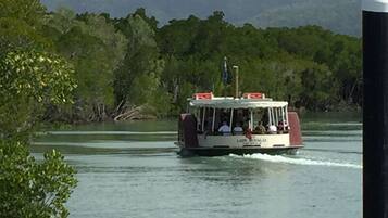 A boat with passengers, moving on a body of water with a forested background.