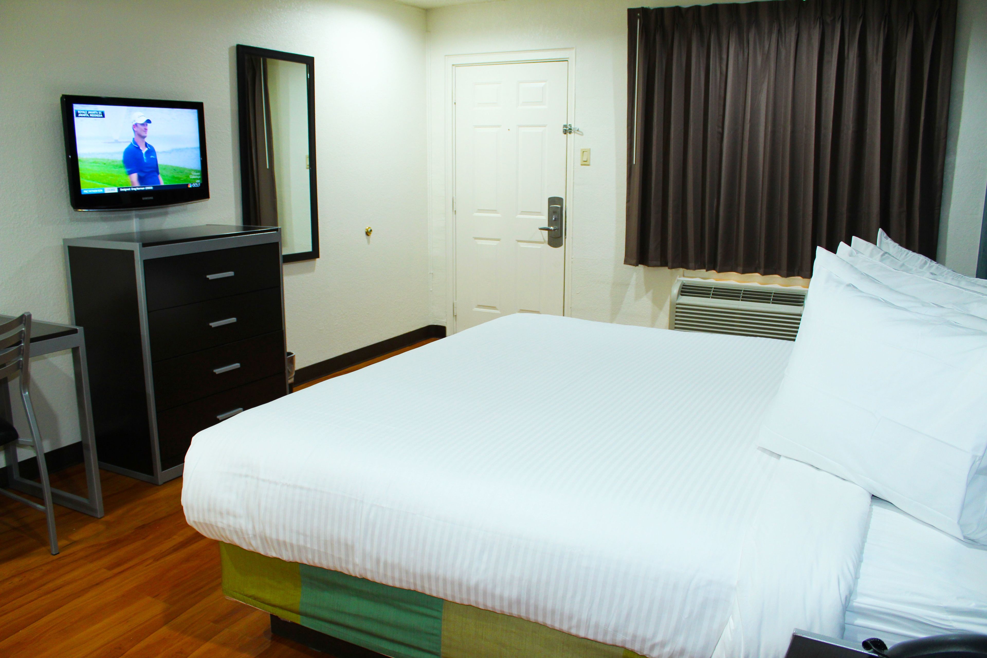 Een hotelkamer met een bed, een aan de muur bevestigde televisie, een dressoir en een deur.