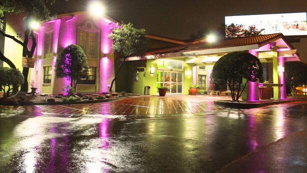 A hotel with a green facade, large windows, and a wet ground reflecting lights. - Stay Express Inn Dallas - Fair Park / Downtown (Dallas)