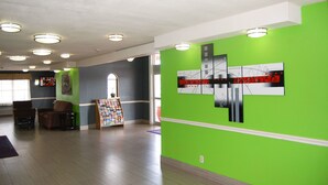 A spacious lobby with a green wall, a large abstract art piece, and a children's book display. - Stay Express Inn Dallas - Fair Park / Downtown (Dallas)