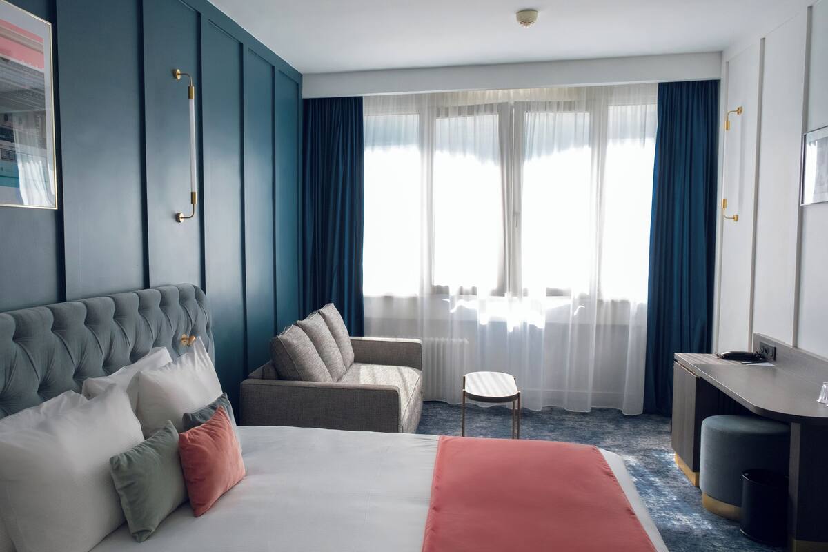 A hotel room with a large bed, a sofa, a small table, and a desk.