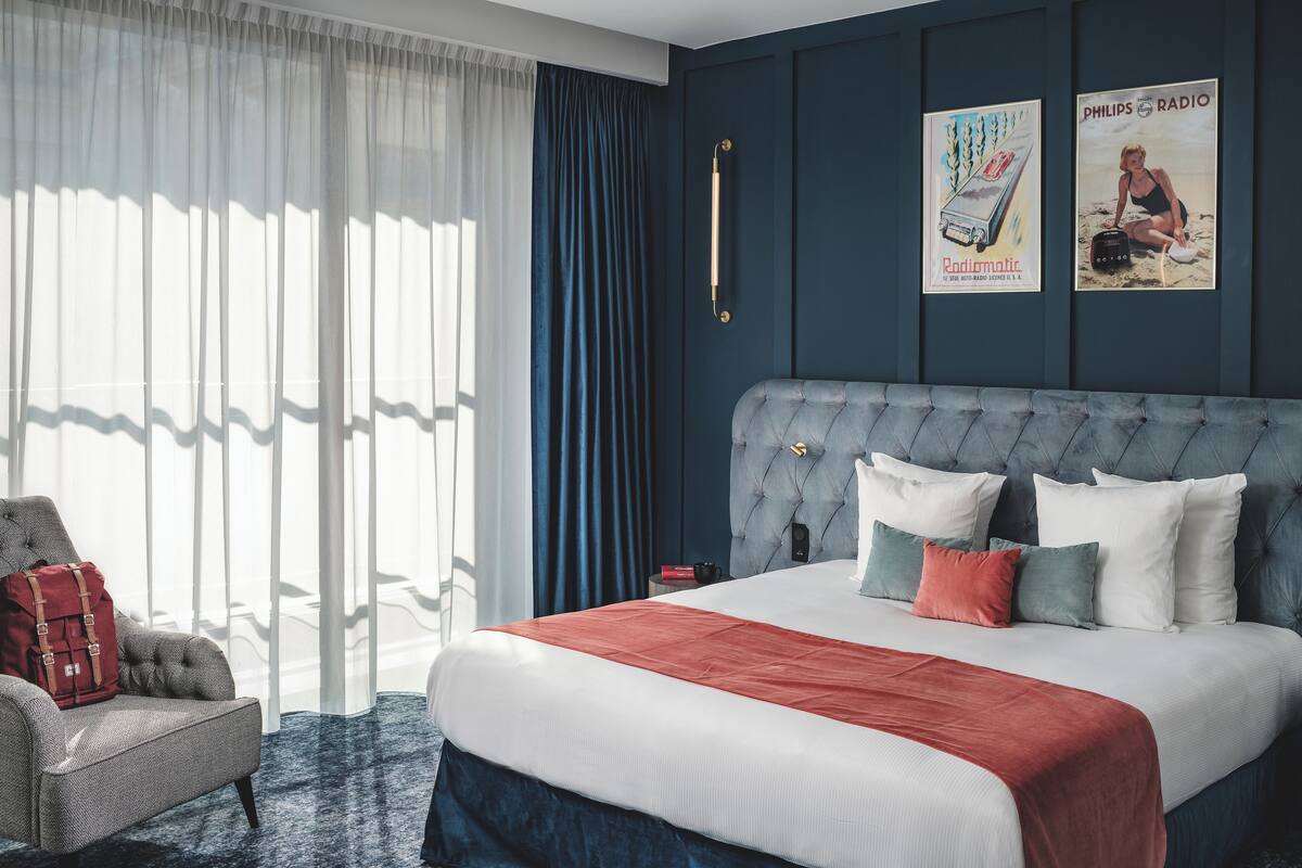 A bedroom with a large bed, a chair, a nightstand, and two posters on the wall.