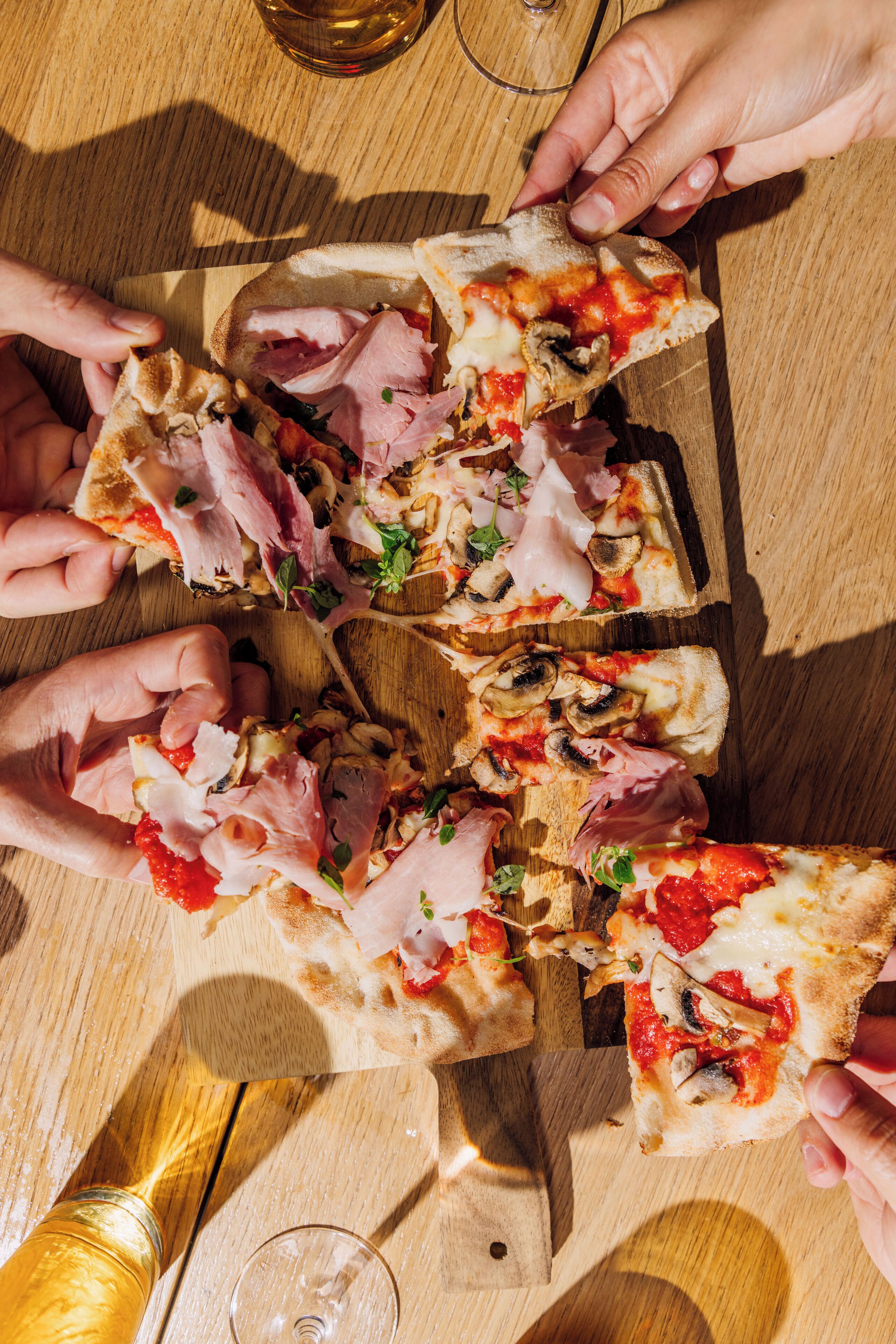 A wooden table with a pizza cut into slices, a glass of wine, and a bottle of wine.