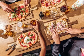 A group of people sharing pizzas on a wooden table with glasses of beer and wine. - Pley Hotel (Paris)