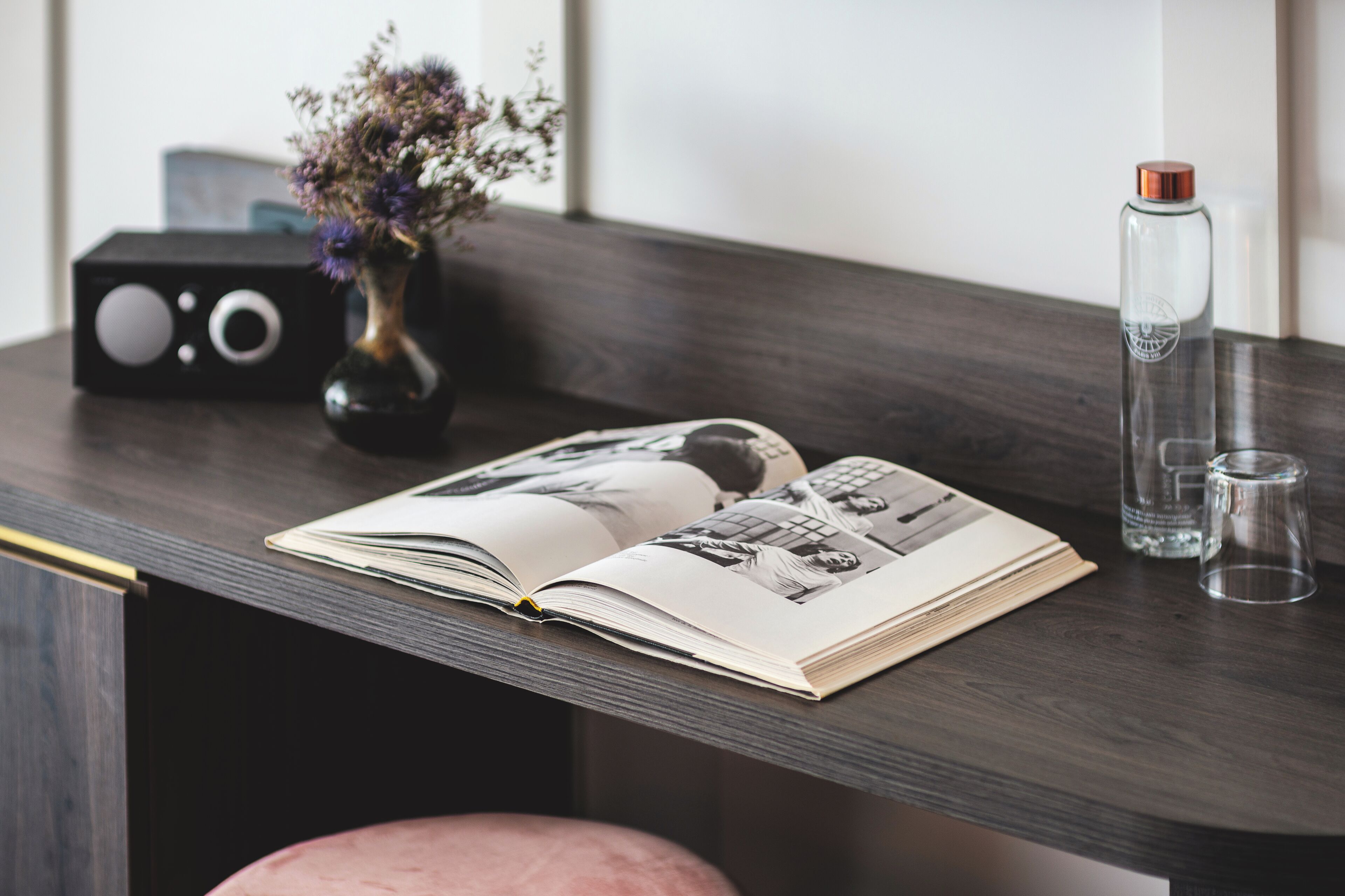 A wooden table with a book, a vase with flowers, a radio, and a water bottle.