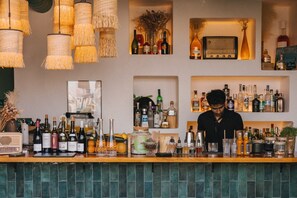 A bar area with shelves of various liquor bottles, a radio, and hanging wicker lamps. - Pley Hotel (Paris)