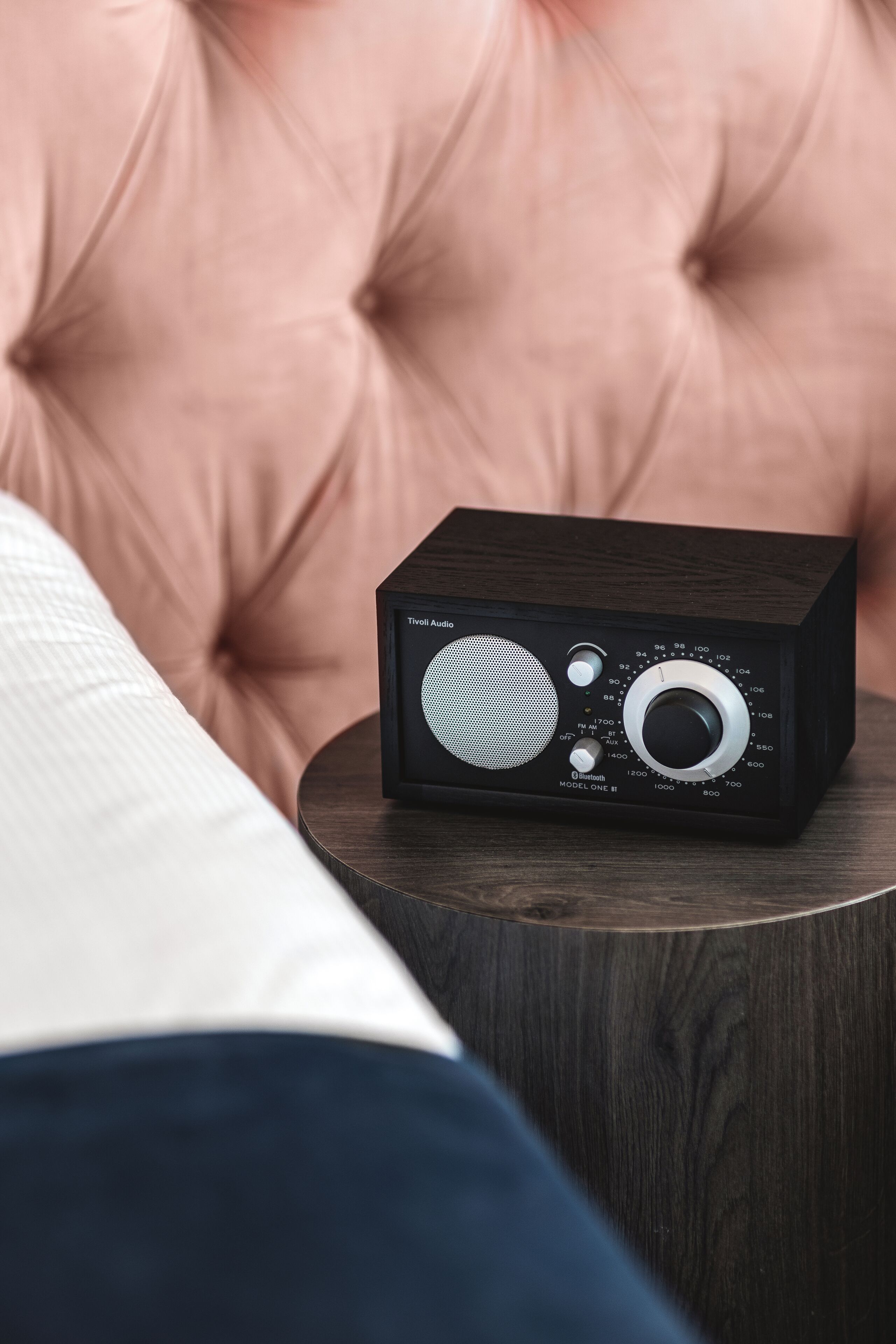 A black radio on a wooden side table next to a tufted pink sofa.