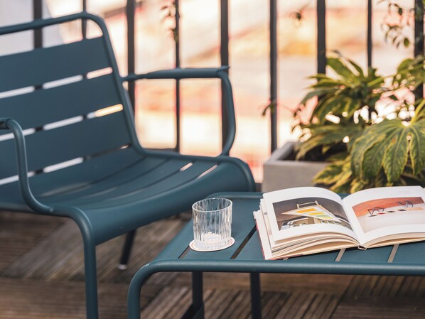 A green metal bench with a glass and a magazine on it.