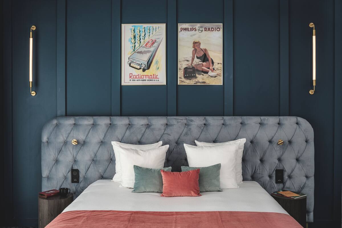 A bedroom with a tufted headboard, a bed with white and red bedding, two bedside tables, and two wall-mounted light fixtures.