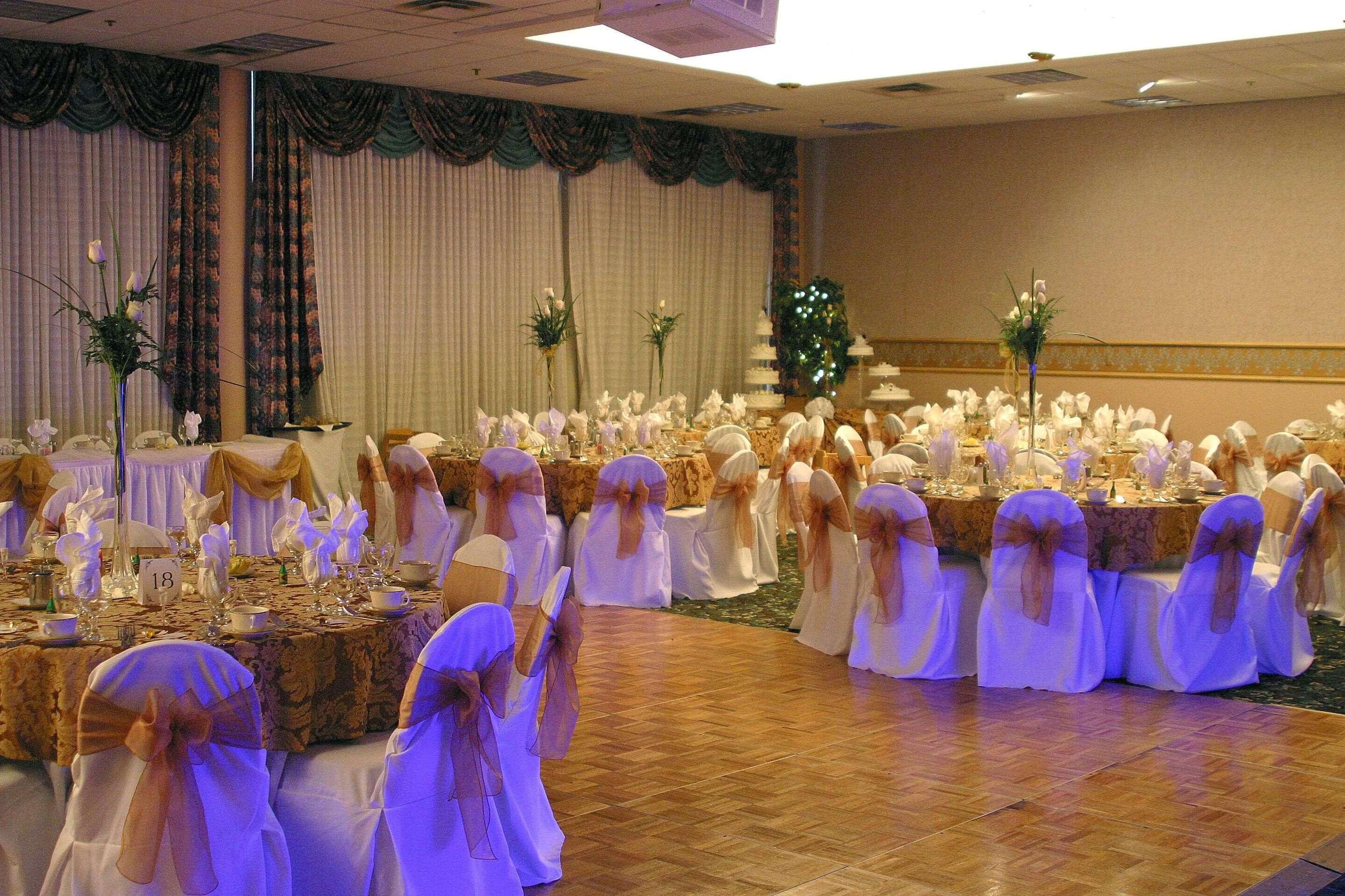 A banquet hall with round tables, white tablecloths, and chairs with white sashes.