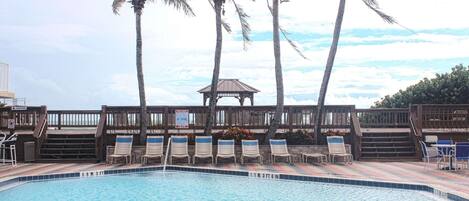 A pool area with lounge chairs, a gazebo, and palm trees.