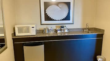 Una kitchenette compacta con microondas, cafetera y lavamanos.