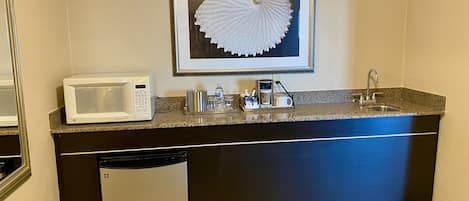 A compact kitchenette with a microwave, coffee maker, and sink.