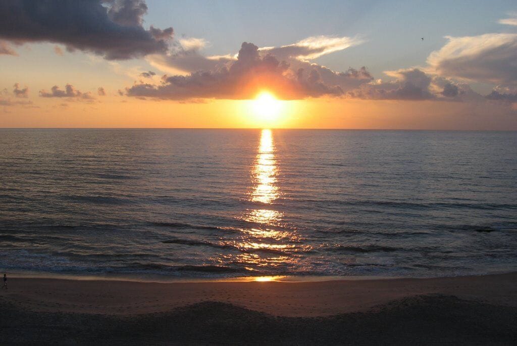 A sunset over a calm sea with a beach in the foreground.
