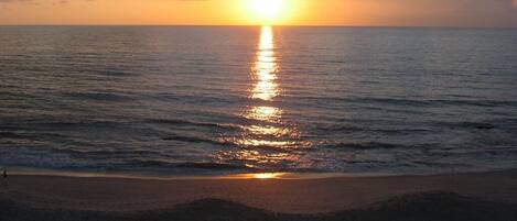 A sunset over a calm sea with a beach in the foreground.
