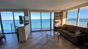 Amplia sala de estar con sofá, una mesita de centro y televisor. Cuenta con ventanas grandes que ofrecen vistas al mar.