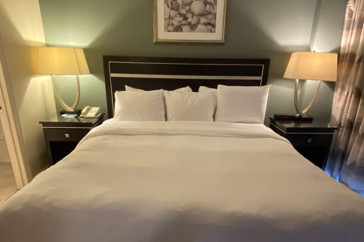 A neatly made bed with white linens, a headboard, and two bedside tables with lamps and a phone.