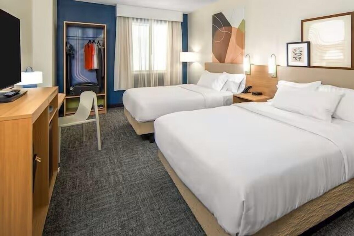 Une chambre d’hôtel avec deux lits, un bureau, une chaise et une armoire.