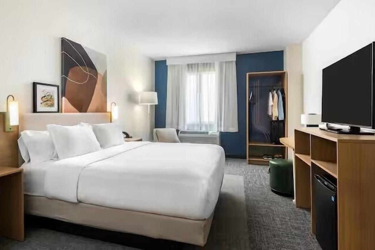 Une chambre d’hôtel avec un grand lit, des tables de chevet, une télévision, une armoire et une fenêtre avec des rideaux.