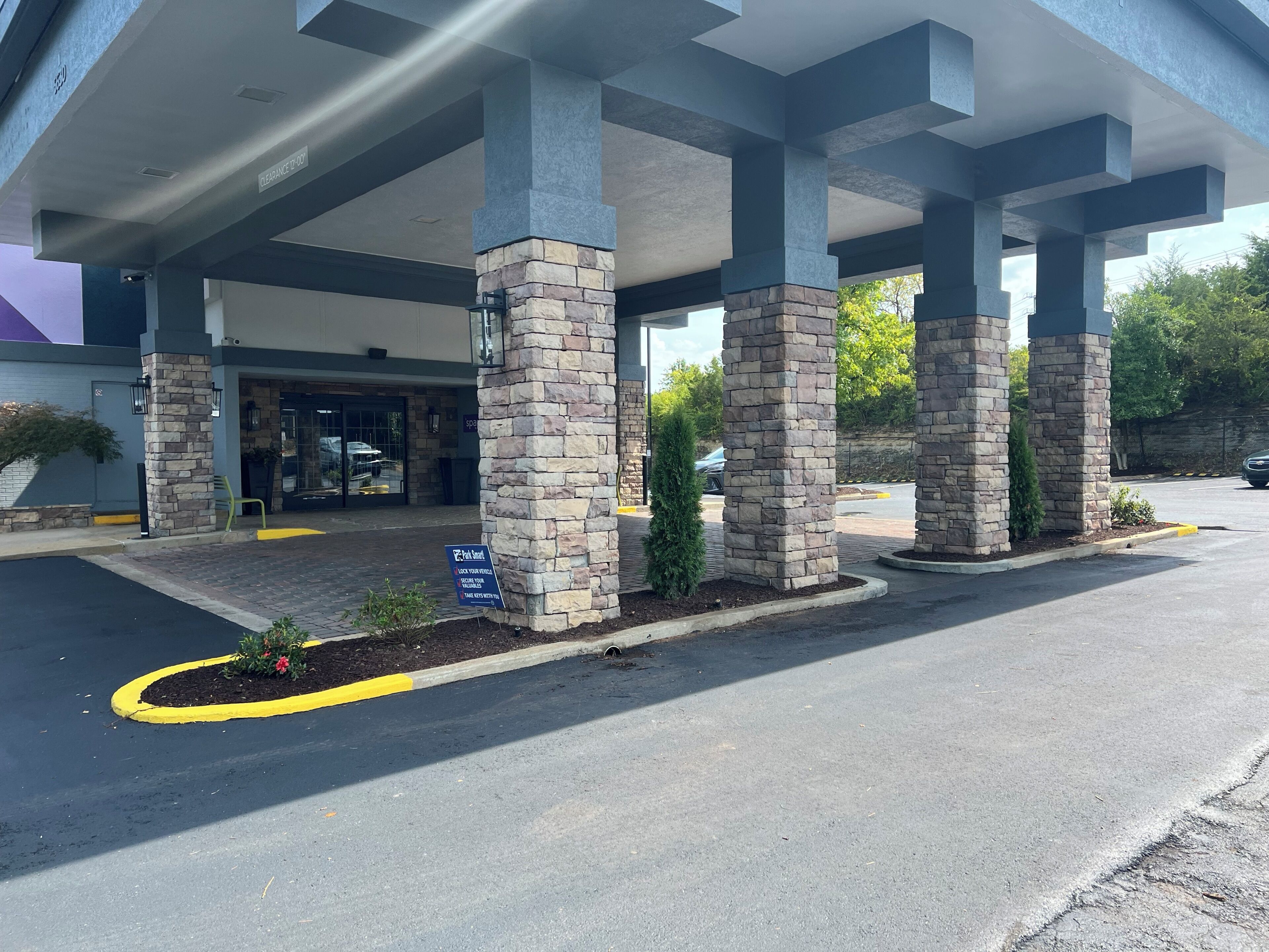 A building entrance with stone pillars, a clear sky, and a parking area.