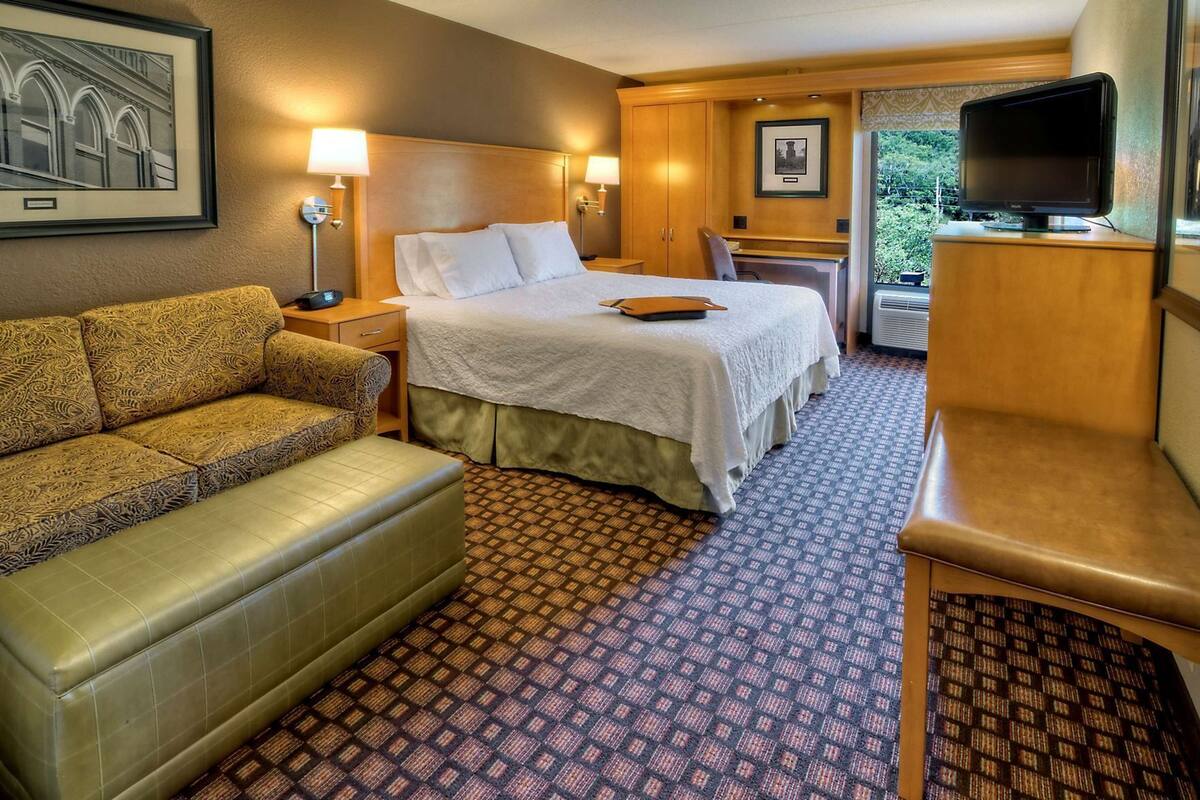Een hotelkamer met een bed, een bank, een bureau, een televisie en een lijst op de muur.