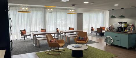 A modern hotel room with a dining area, a coffee station, and a seating area with a coffee table.