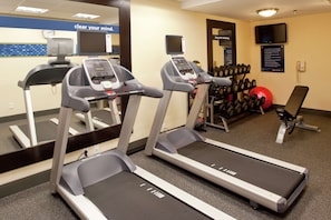 Une salle de sport équipée de tapis de course, d’un banc de musculation, d’haltères et de ballons d’exercice.