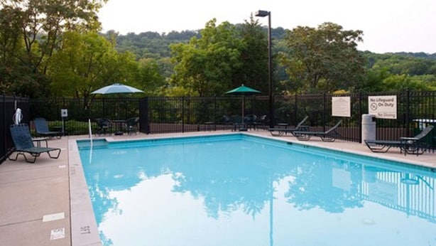 Une piscine entourée d’une clôture et d’arbres, avec des chaises longues et des parasols.