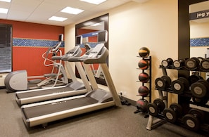 Une salle de sport équipée de tapis de course, d’un grand miroir fixé au mur et d’un porte-haltères.