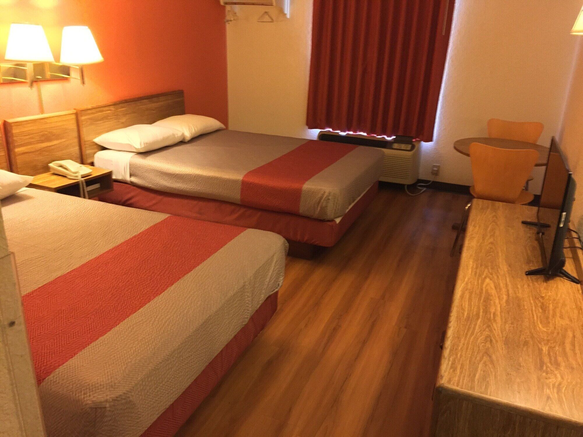 A hotel room with two beds, a desk, a chair, a telephone, and a window with curtains.