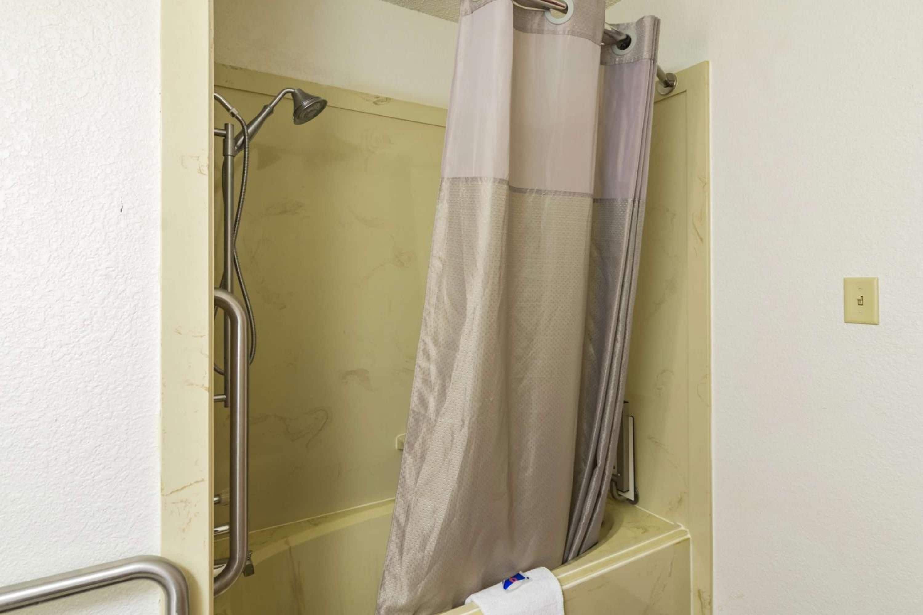 Un baño con ducha, barra de apoyo y perchero.