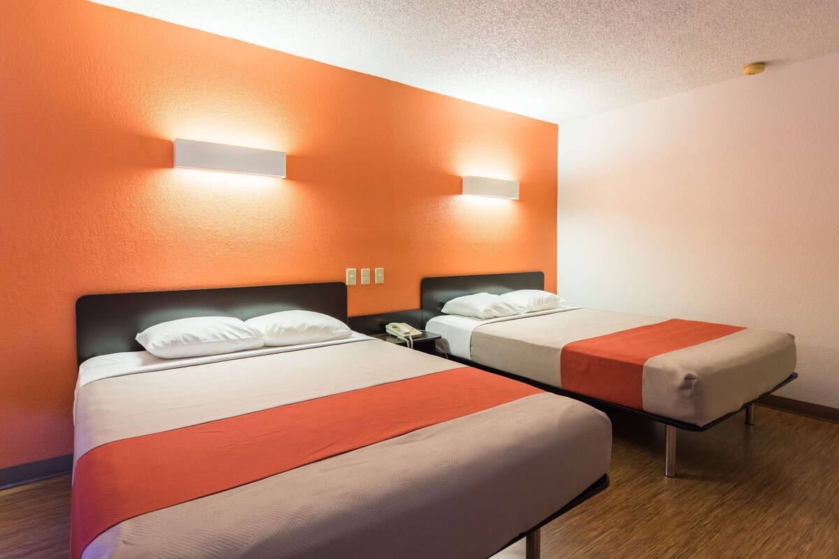 A hotel room with two beds, each with a white and orange bedspread, and a nightstand with a phone.