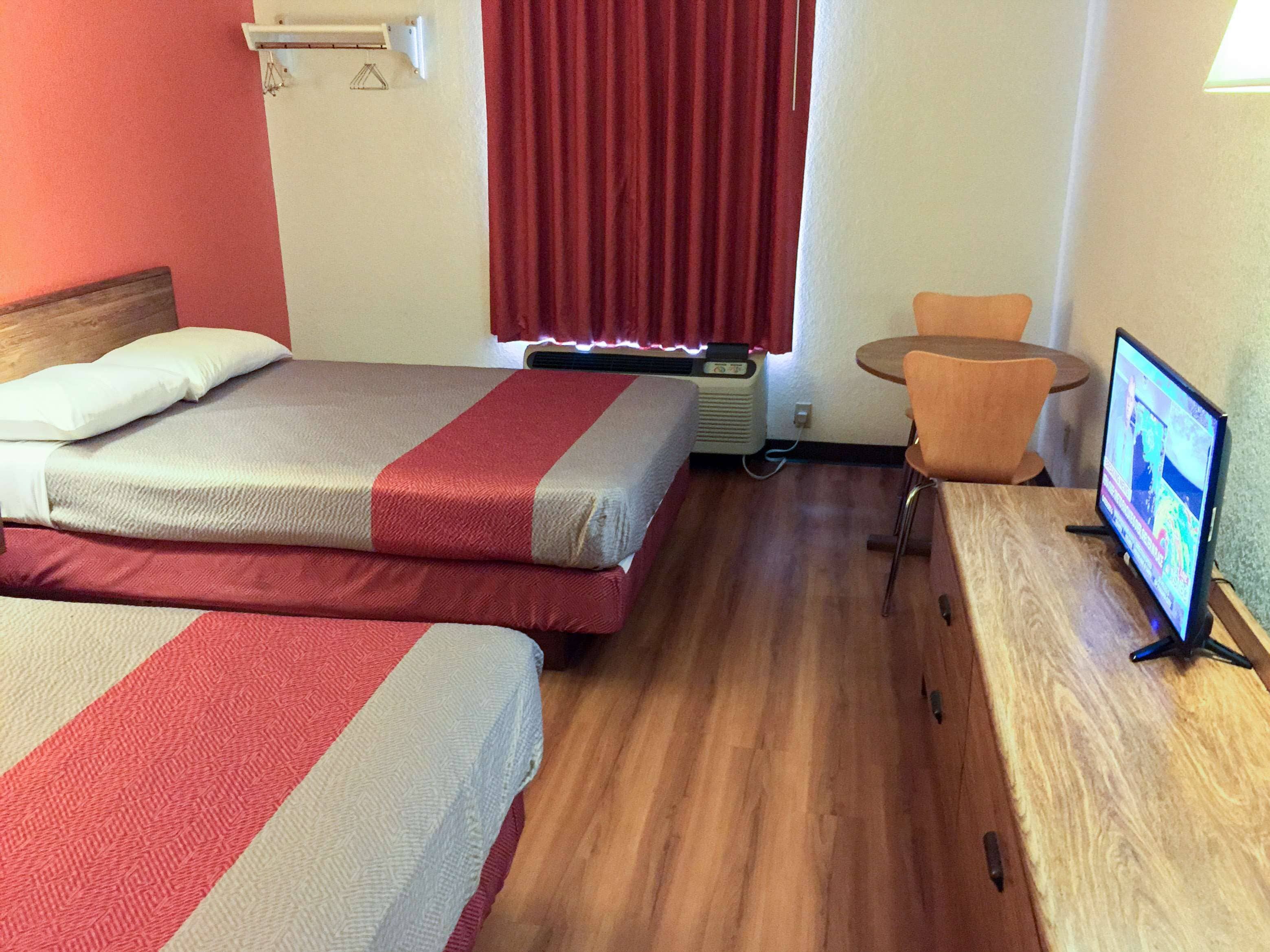 A hotel room with two beds, a desk with a computer, a chair, and a window with curtains.