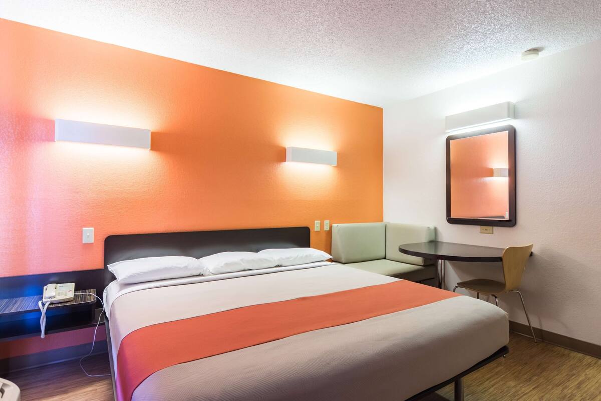 A hotel room with a bed, a desk, a chair, and a small table.