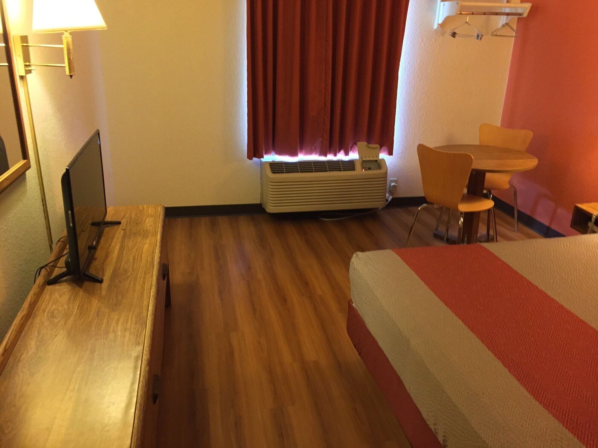 A hotel room with a bed, a desk, a chair, a table, a lamp, and a window with curtains.