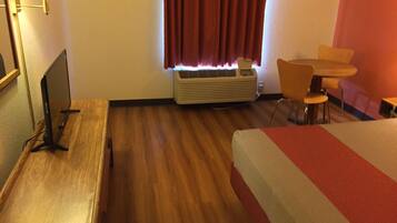 A hotel room with a bed, a desk, a chair, a table, a lamp, and a window with curtains.