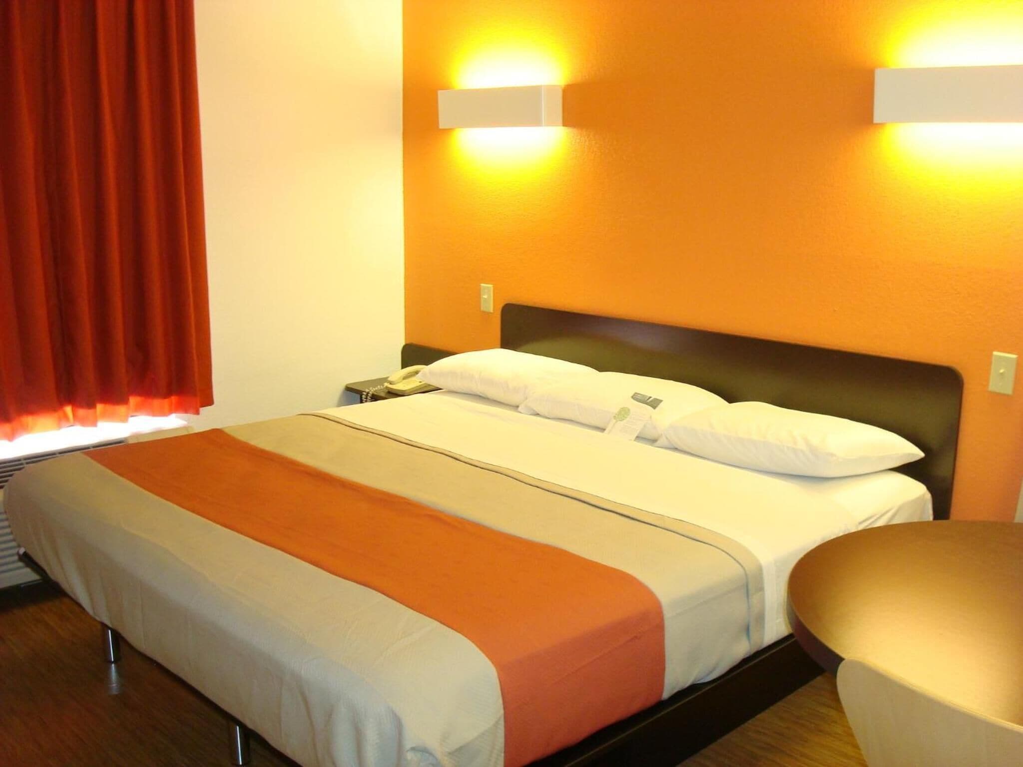 Una habitació d'hotel amb un llit, una taula de nit, un telèfon i una làmpada penjada a la paret.