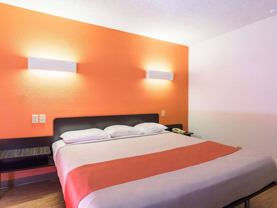A hotel room with a bed, a nightstand, and two wall-mounted lights.
